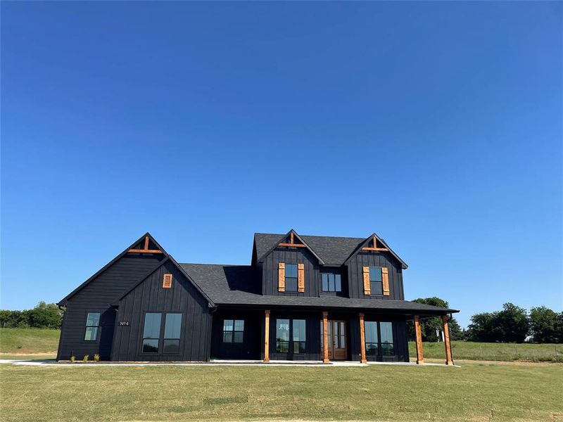Modern farmhouse exterior featuring dark vertical siding, multiple gables, natural wood window shutters, a covered front porch with timber posts, and large picture windows
