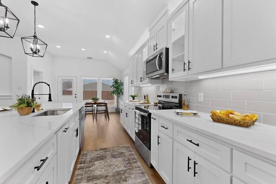 Kitchen featuring vaulted ceiling, white cabinetry, stainless steel appliances, light stone counters, and dark wood-style floors Kitchen featuring vaulted ceiling, white cabinetry, stainless steel appliances, light stone counters, and dark wood-style floors