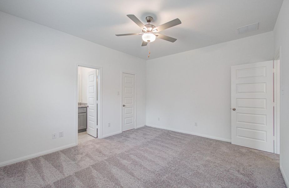 Spacious bedroom with plush carpeting, a ceiling fan, and ample natural light, featuring convenient access to an en-suite bathroom.