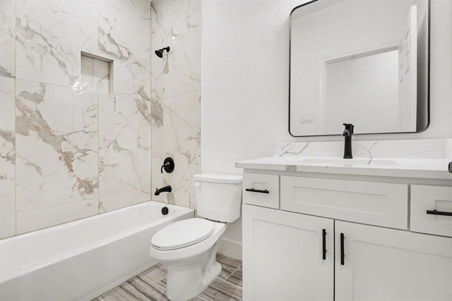 Bathroom featuring a bathtub with a shower, a toilet, and a vanity with a white countertop