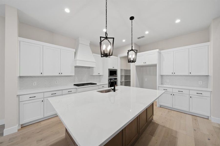 Kitchen with decorative backsplash, white cabinetry, hanging light fixtures, light stone counters, and a kitchen island with sink Kitchen with decorative backsplash, white cabinetry, hanging light fixtures, light stone counters, and a kitchen island with sink