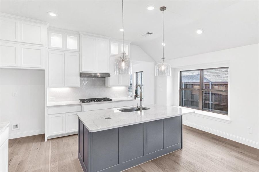 Kitchen with light stone countertops, sink, decorative light fixtures, a kitchen island with sink, and white cabinets