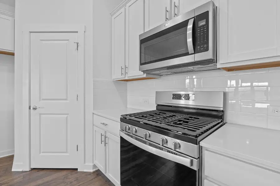Kitchen featuring stainless steel appliances, tasteful backsplash, white cabinetry, and dark wood-type flooring Kitchen featuring stainless steel appliances, tasteful backsplash, white cabinetry, and dark wood-type flooring