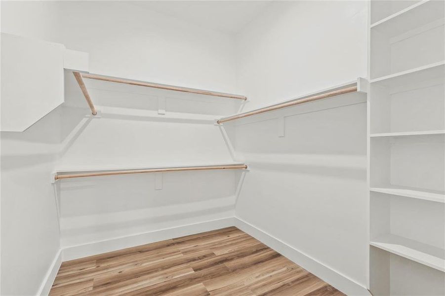 Walk-in closet featuring wood-finish flooring, white walls, multiple hanging rods, shelving units, and built-in storage