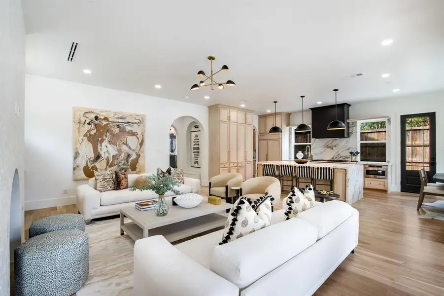 Open-concept living area featuring light wood-finish flooring, recessed lighting, a modern chandelier, and an arched entryway Open-concept living area featuring light wood-finish flooring, recessed lighting, a modern chandelier, and an arched entryway