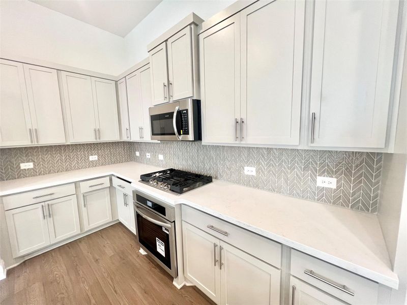 Kitchen with tasteful backsplash, appliances with stainless steel finishes, light countertops, and light wood finished floors Kitchen with tasteful backsplash, appliances with stainless steel finishes, light countertops, and light wood finished floors