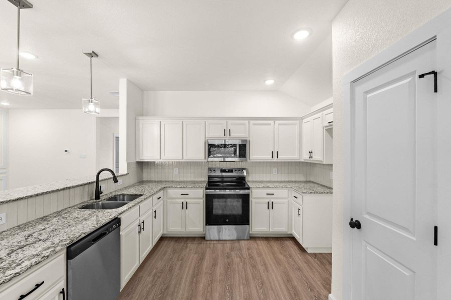 Kitchen with stainless steel appliances, white cabinetry, pendant lighting, backsplash, and vaulted ceiling
