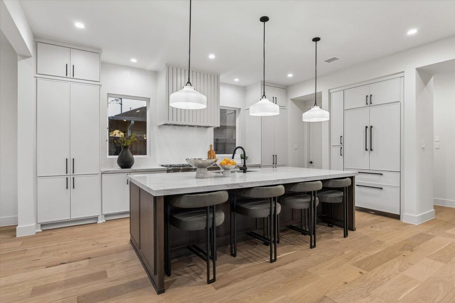 The striking kitchen is equipped with premium Thermador appliances, including double ovens, a 6-burner gas range with griddle, a paneled refrigerator and dishwasher, and a custom range hood.