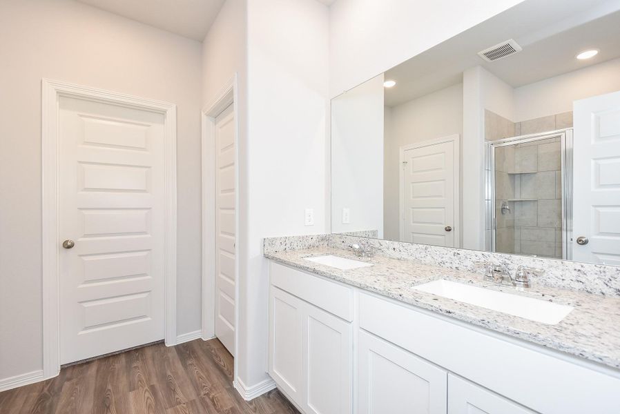 Snowy white cabinetry hosts dual sinks; with shining wall-wide mirror in your primary ensuite bathroom. Reflected in the mirror is a comfortable walk-in, glass enclosed shower. Snowy white cabinetry hosts dual sinks; with shining wall-wide mirror in your primary ensuite bathroom. Reflected in the mirror is a comfortable walk-in, glass enclosed shower.