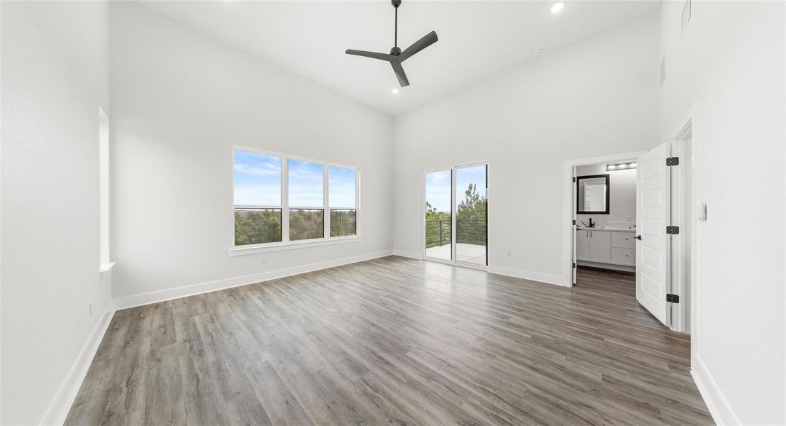 Unfurnished bedroom featuring access to outside, a towering ceiling, light wood finished floors, ceiling fan, and recessed lighting