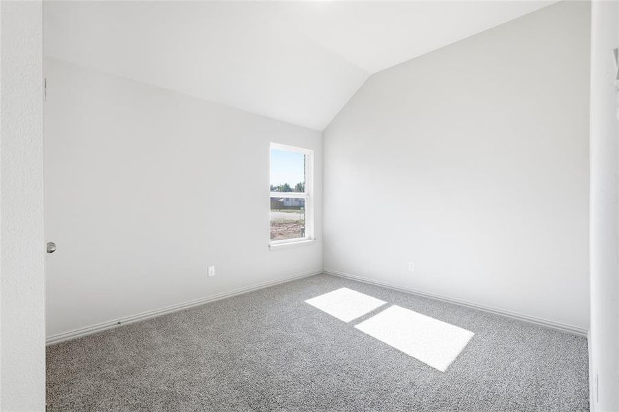 Carpeted spare room featuring vaulted ceiling and baseboards
