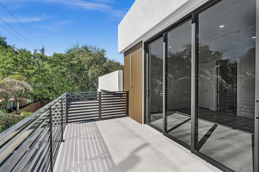 Covered balcony featuring concrete flooring, horizontal slat metal railing, expansive sliding glass doors, and recessed ceiling lighting Covered balcony featuring concrete flooring, horizontal slat metal railing, expansive sliding glass doors, and recessed ceiling lighting