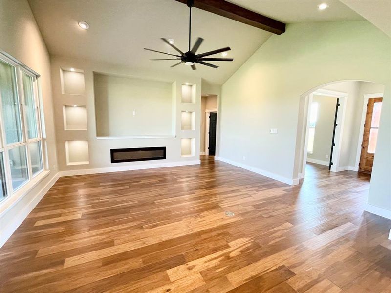 Unfurnished living room featuring ceiling fan, beam ceiling, high vaulted ceiling, and light hardwood / wood-style flooring