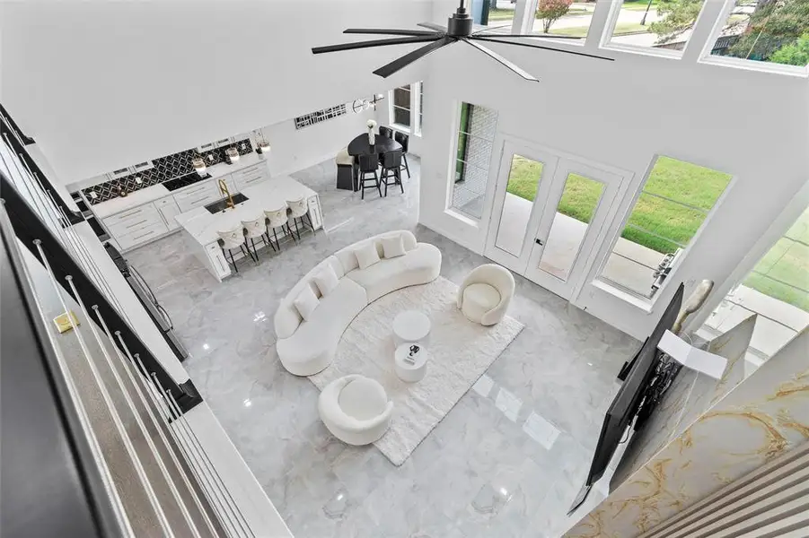 Two-story living area featuring a vaulted ceiling with a large ceiling fan, a full wall of windows, and a gourmet kitchen