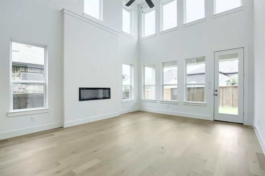 Spacious living area featuring a double-height ceiling, wood-finish flooring, and a linear electric fireplace