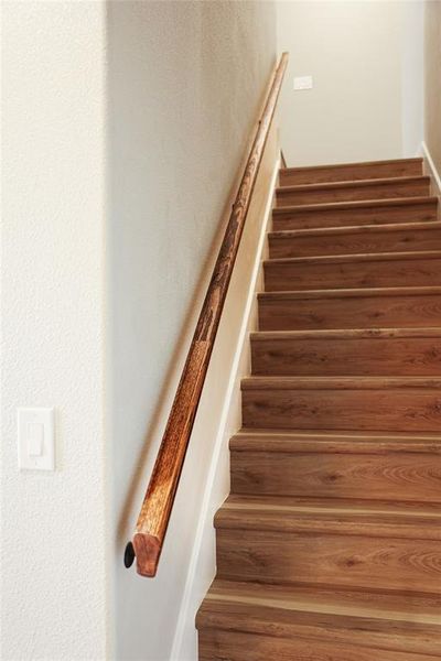 Staircase featuring wood-finish treads and risers, complemented by a solid wood handrail, and light-toned wall finishes