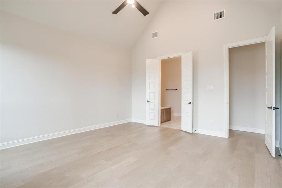 Unfurnished bedroom with ceiling fan, light wood-type flooring, ensuite bathroom, and high vaulted ceiling