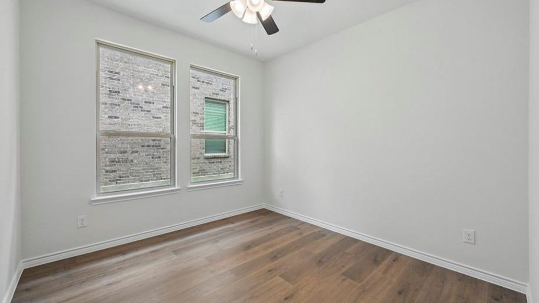 Bright interior room featuring a ceiling fan with integrated lighting, wood-finish flooring, two windows with white trim, and light-toned wall paint