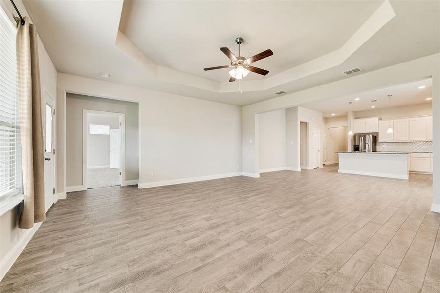 Unfurnished living room with a raised ceiling, light wood-type flooring, and ceiling fan
