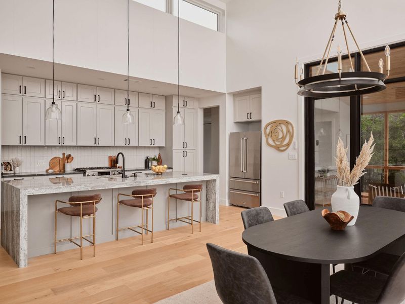 Open-concept kitchen and dining area featuring a waterfall island with stone countertop, light-toned wood-finish flooring, and a full suite of stainless steel appliances