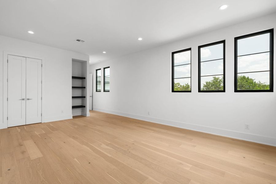 Blonde hardwood floors grace this naturally illuminated room, featuring large windows and built-in shelving.