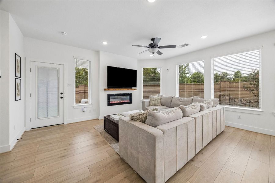 Cozy up in the light-filled living room featuring an electric fireplace, recessed lighting, oversized windows, and an open-concept layout. Enjoy seamless access to the covered backyard patio, perfect for relaxing or entertaining.