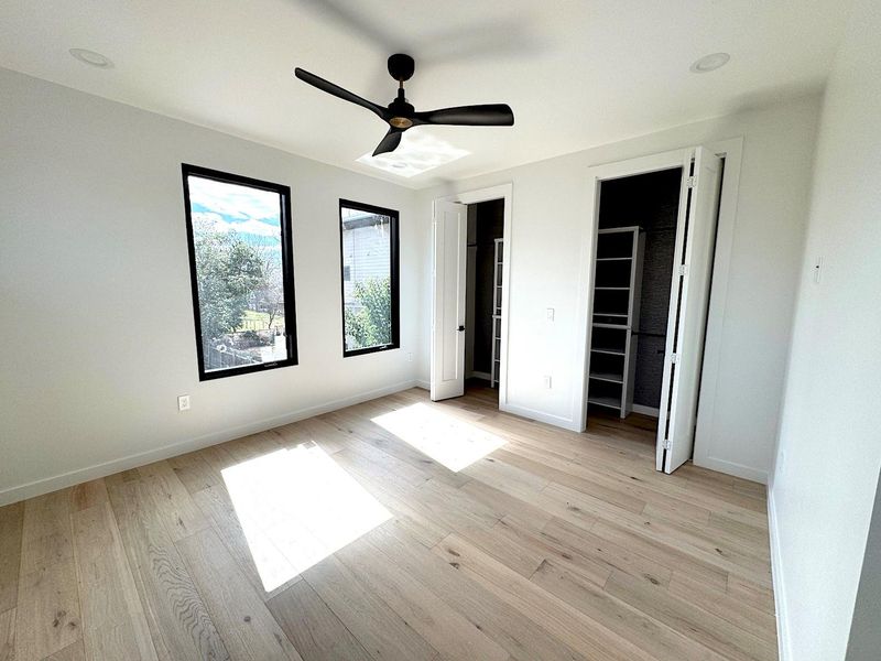 Unfurnished bedroom featuring two closets, baseboards, light wood finished floors, and ceiling fan