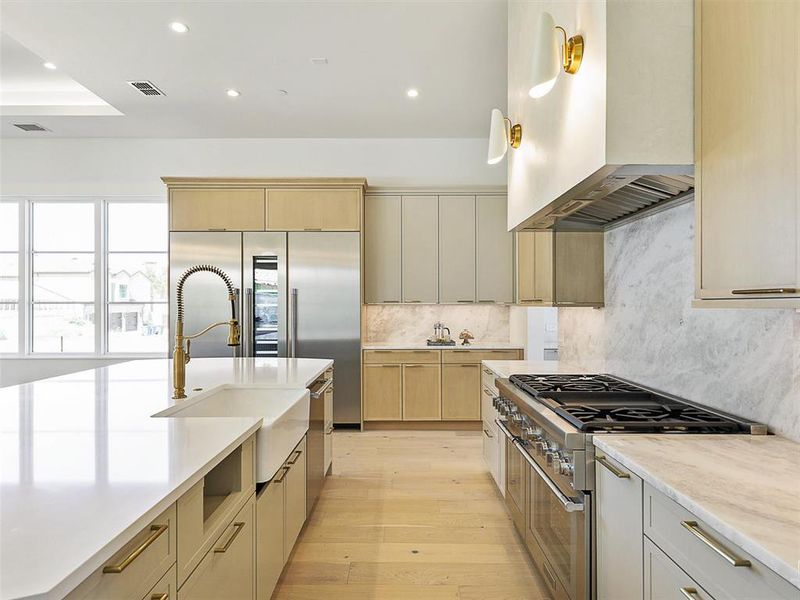 Kitchen with decorative backsplash, light hardwood / wood-style floors, high quality appliances, sink, and wall chimney range hood