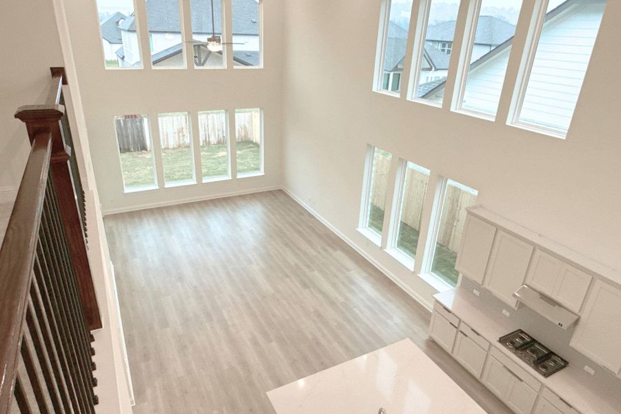 Unfurnished living room featuring a high ceiling, light wood-style flooring, ceiling fan, and plenty of natural light