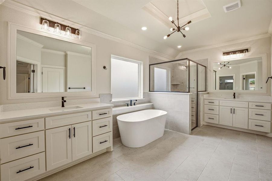 Bathroom featuring a freestanding tub, a stall shower, two vanities, hanging lights, and ornamental molding