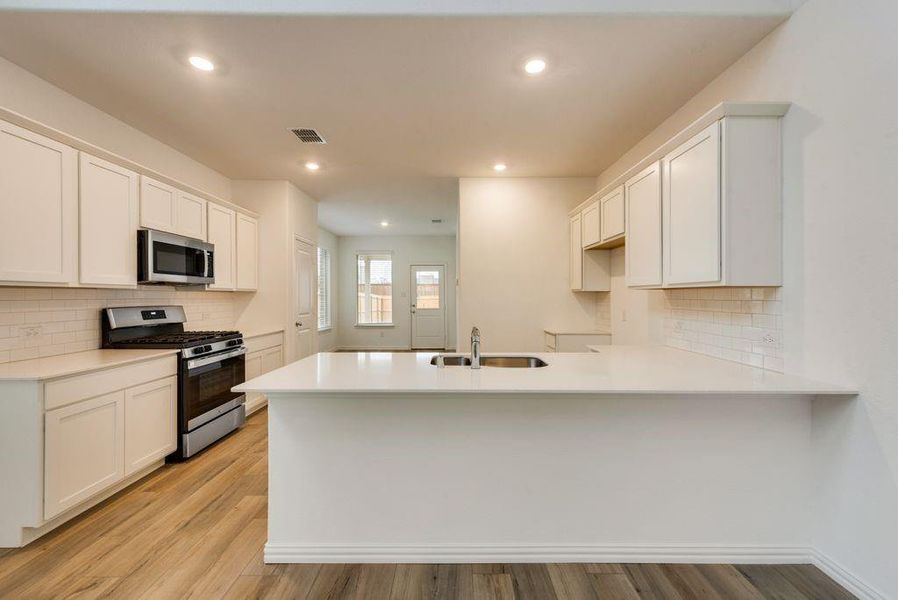 Kitchen with backsplash, light hardwood / wood-style flooring, appliances with stainless steel finishes, white cabinetry, and kitchen peninsula