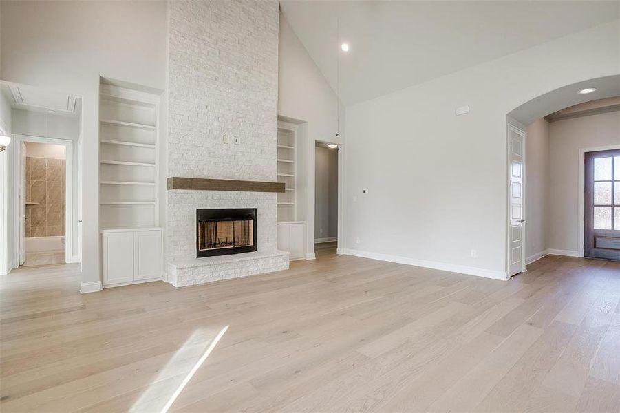 Unfurnished living room featuring a stone fireplace, built in shelves, high vaulted ceiling, and light hardwood / wood-style floors