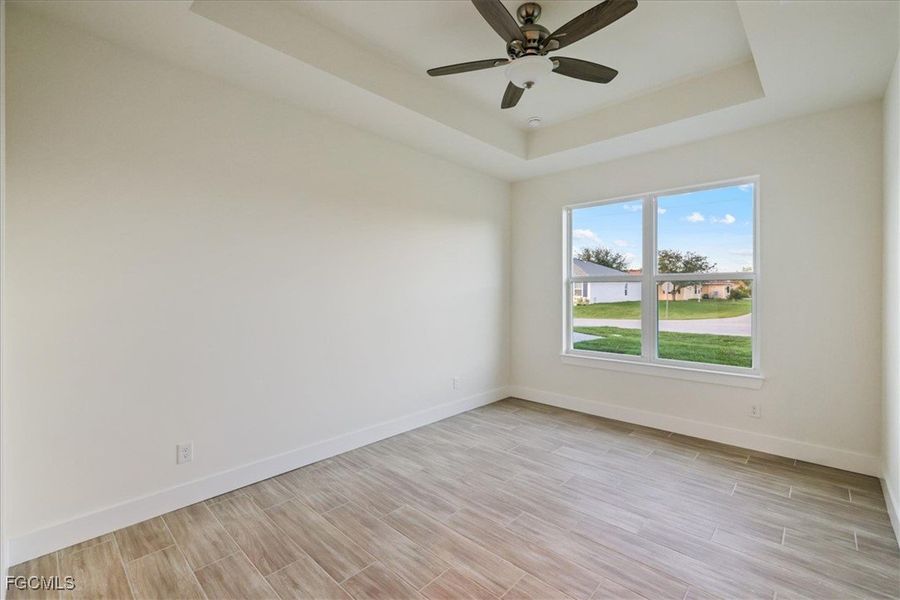Empty room with a tray ceiling, wood tiled floors, and a ceiling fan