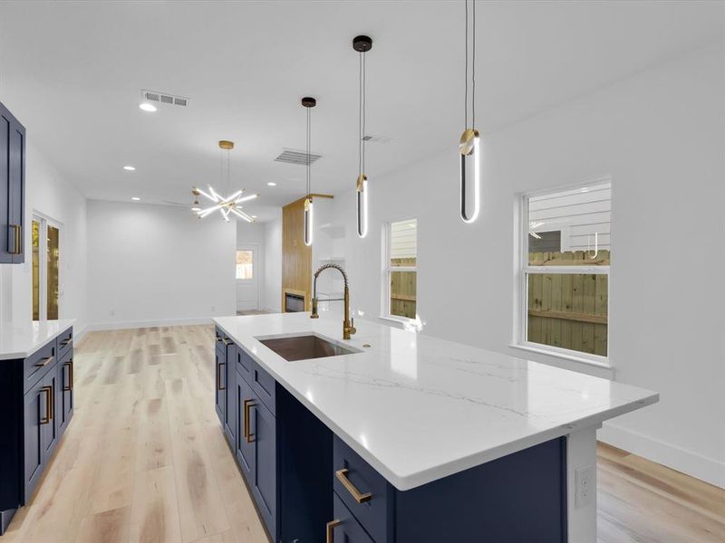 Kitchen featuring light wood-type flooring, sink, blue cabinetry, hanging light fixtures, and an island with sink