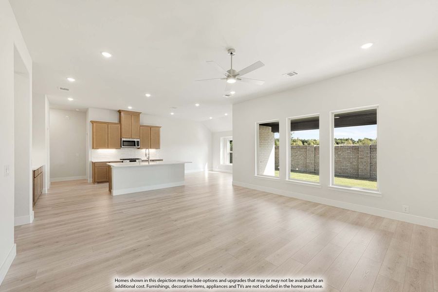 Open living area with light wood floors, ceiling fan, and kitchen with wood cabinets and white island in background Open living area with light wood floors, ceiling fan, and kitchen with wood cabinets and white island in background