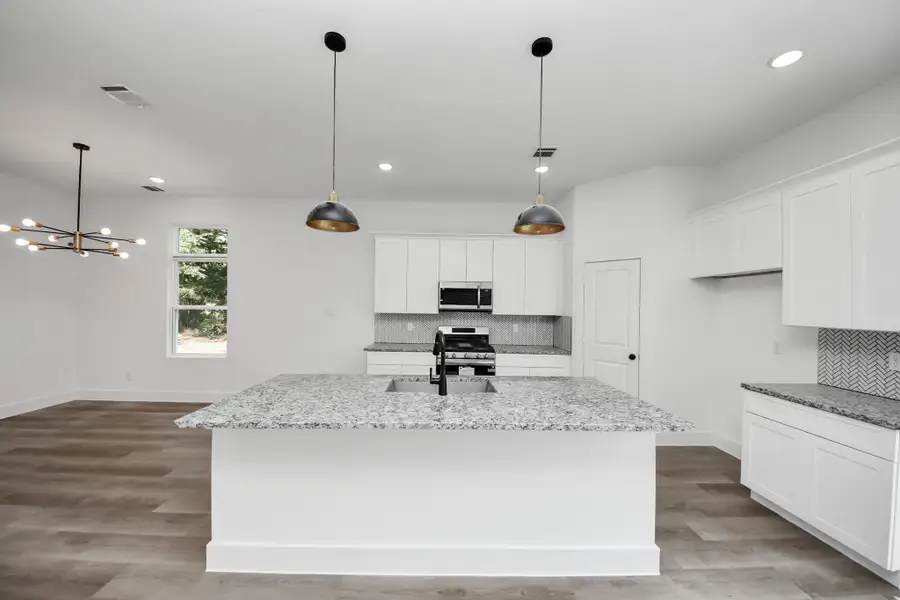 Spacious open-concept kitchen with large island, granite countertops, white cabinetry, and modern pendant lighting
