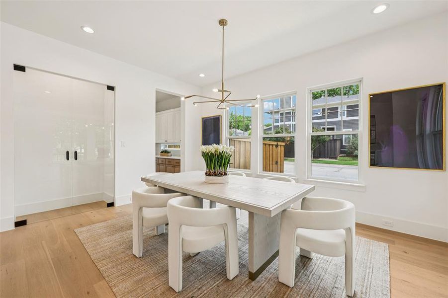 Open-concept dining area featuring wood-finish flooring, a modern linear chandelier, recessed lighting, and three large windows