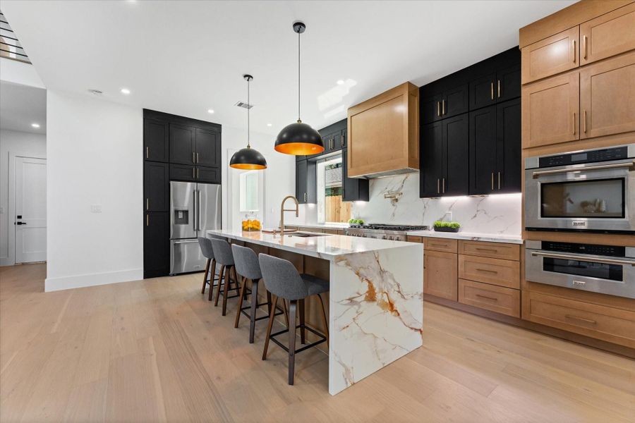 This kitchen features a modern design with a large Silestone island, sleek black and wood cabinetry, professional stainless-steel appliances, and stylish pendant lighting. Perfect for entertaining and culinary enthusiasts. This kitchen features a modern design with a large Silestone island, sleek black and wood cabinetry, professional stainless-steel appliances, and stylish pendant lighting. Perfect for entertaining and culinary enthusiasts.