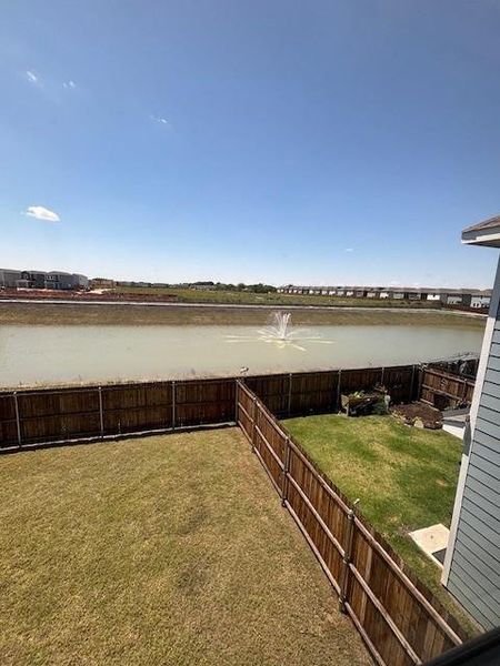 Expansive backyard featuring a manicured lawn, wood fencing, and a water feature