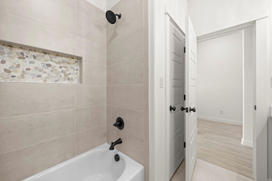 A well-appointed bath features a tiled shower and built-in niche with pebble accents.