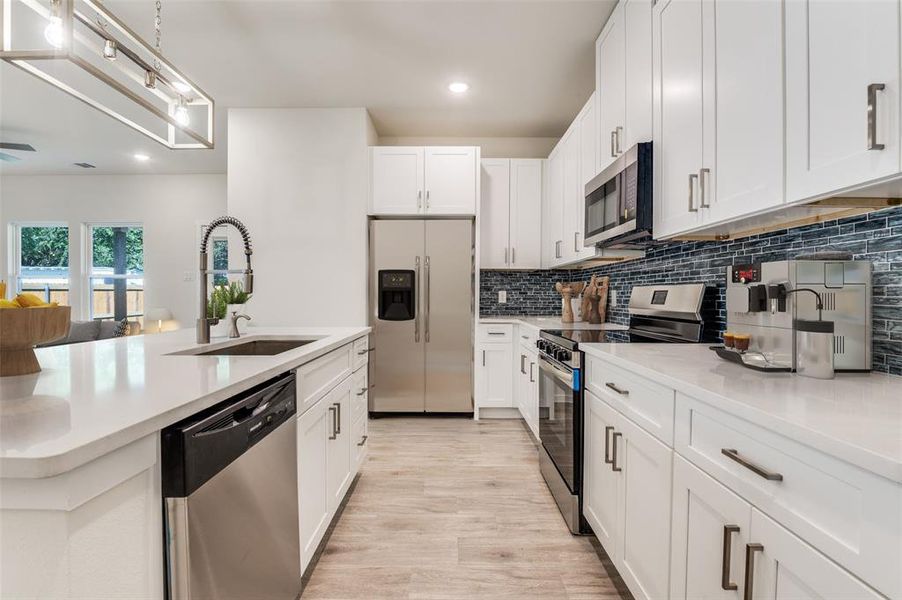 Kitchen featuring stainless steel appliances, white cabinetry, backsplash, open floor plan, and recessed lighting