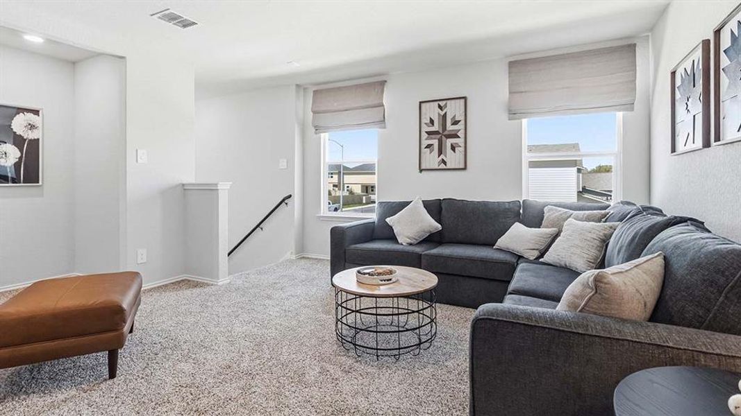 Carpeted loft space featuring light neutral wall tones, multiple windows with window treatments, and a half-wall banister