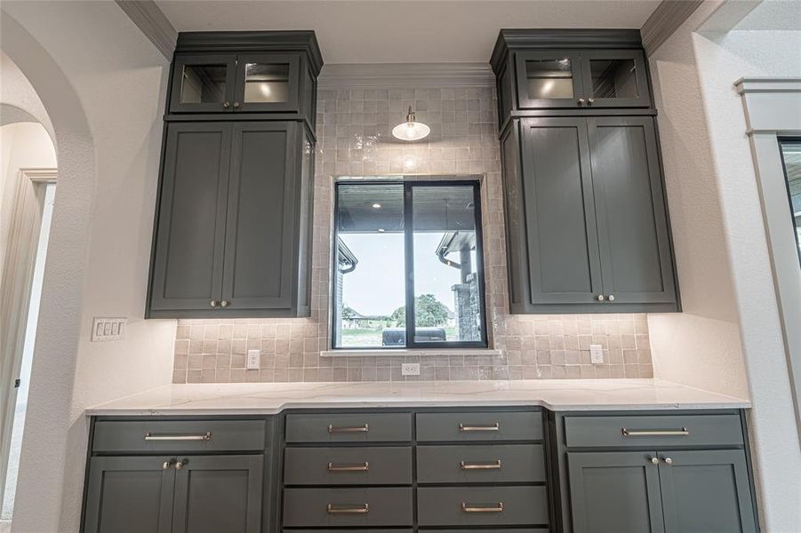 Kitchen with gray cabinets, light stone countertops, glass insert cabinets, ornamental molding, and arched walkways Kitchen with gray cabinets, light stone countertops, glass insert cabinets, ornamental molding, and arched walkways