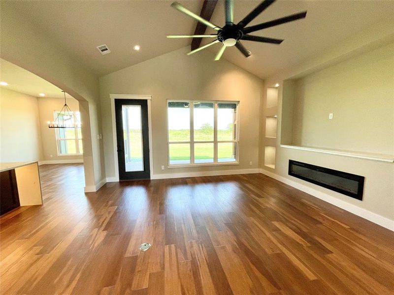 Unfurnished living room featuring high vaulted ceiling, ceiling fan with notable chandelier, and wood-type flooring