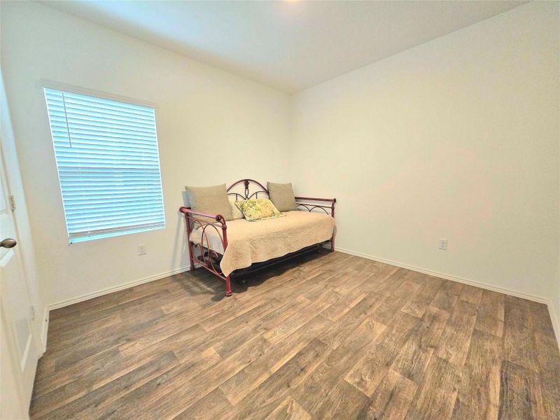 Spacious room featuring wood-finish flooring, white baseboards, and a single window with blinds