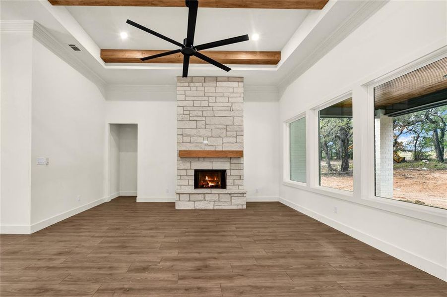 Unfurnished living room featuring beam ceiling, ceiling fan, a stone fireplace, dark wood finished floors, and coffered ceiling Unfurnished living room featuring beam ceiling, ceiling fan, a stone fireplace, dark wood finished floors, and coffered ceiling