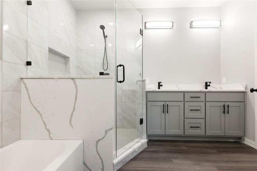 Full bathroom with double vanity, a marble finish shower, a bath, and dark wood-type flooring