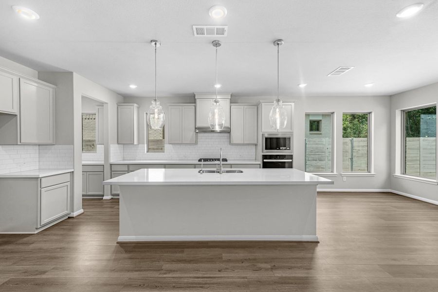 Luxury light and bright kitchen with upgraded lighting and views of the trees neighboring you behind.