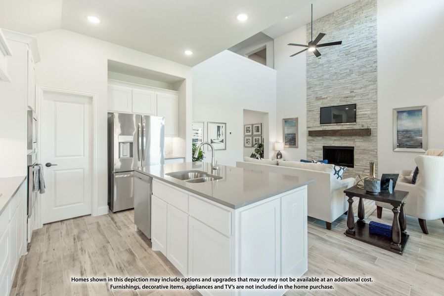 Open-concept kitchen with white island and gray countertop flowing into living room with stone fireplace and high ceilings
