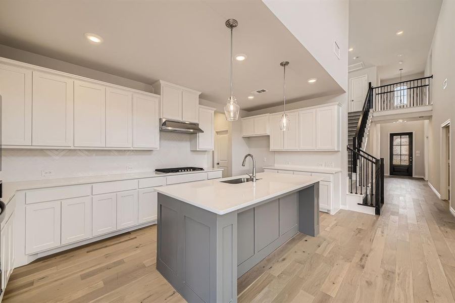 Kitchen with a center island with sink, sink, pendant lighting, white cabinetry, and light hardwood / wood-style floors